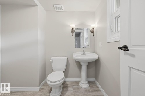 Pedestal sink with wall-mounted sconces, framed mirror, and panel door with dark hardware - 10621 Beaumaris Road Nw, Edmonton, AB 