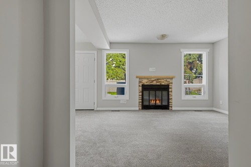 Carpeted living space featuring a fireplace with a stacked stone surround and two windows - 10621 Beaumaris Road Nw, Edmonton, AB 