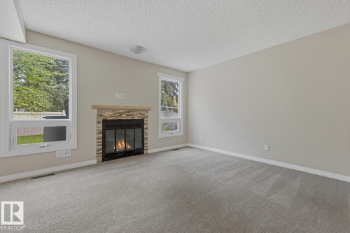 Recessed fireplace with stone surround, wood mantel, and large windows - 10621 Beaumaris Road Nw, Edmonton, AB 