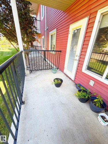 Concrete patio with black metal railings, red horizontal siding, and multiple windows - #118 111 Edwards Dr Southwest, Edmonton, AB 