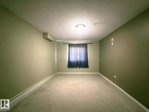 Neutral-toned carpeting, textured ceiling, window with curtain rod, wall-mounted light fixture - #118 111 Edwards Dr Southwest, Edmonton, AB 