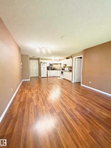 Spacious interior featuring wood-finish flooring, white kitchen cabinetry, and a ceiling-mounted light fixture - #118 111 Edwards Dr Southwest, Edmonton, AB 