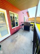 Covered concrete patio with red horizontal siding, white-framed windows, and black metal railing - 