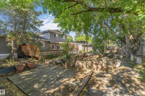 Expansive backyard featuring a multi-level wood deck, mature trees, and natural rock landscaping - 11208 163A Avenue Nw, Edmonton, AB 