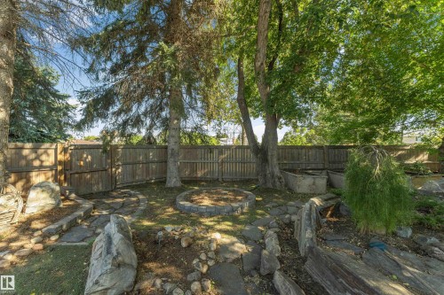 Expansive yard featuring mature trees, a wood privacy fence, a stone-lined fire pit area, and natural stone landscaping elements - 11208 163A Avenue Nw, Edmonton, AB 