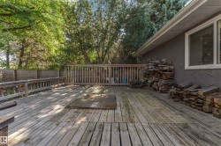 Expansive wood deck with a built-in railing system, featuring a privacy fence and abundant mature trees - 