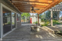 Expansive outdoor decking with a wood pergola, stone fire pit, and ceiling fan - 