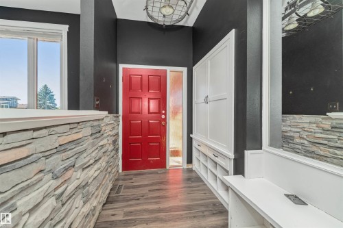 Red panel door entry with transom window, wood-finish flooring, stone accent wall, and built-in white cabinetry with integrated storage - 11208 163A Avenue Nw, Edmonton, AB 