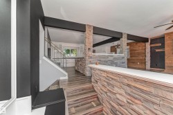 Stone-clad accent walls, wood-finish flooring, a built-in bar with a solid surface countertop, and a contemporary railing system - 