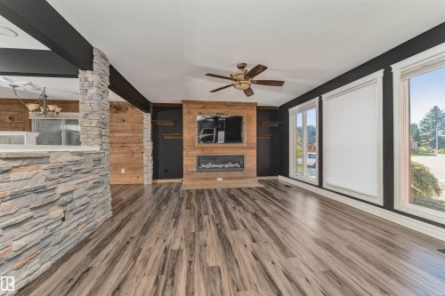 Wood-finish flooring throughout, stone-clad architectural elements, wood-paneled feature wall with built-in fireplace, ceiling fan with integrated lighting, and multiple windows - 11208 163A Avenue Nw, Edmonton, AB 