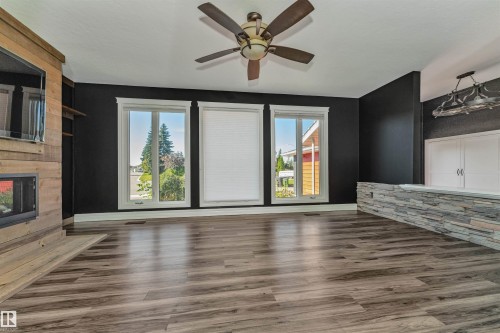 Wood-finish flooring, three large windows, a built-in fireplace with a wood-finish surround, a ceiling fan, and a stone-clad half-wall with a built-in cabinet - 11208 163A Avenue Nw, Edmonton, AB 