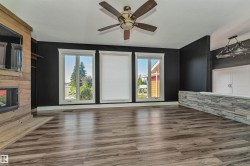 Wood-finish flooring, three large windows, a built-in fireplace with a wood-finish surround, a ceiling fan, and a stone-clad half-wall with a built-in cabinet - 