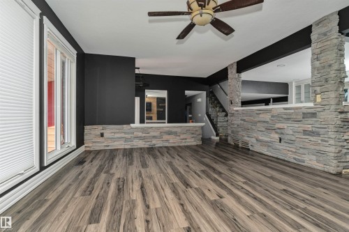Wood-finish flooring, stone-clad half walls, ceiling fan fixture, and white window trim - 11208 163A Avenue Nw, Edmonton, AB 