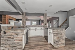 Kitchen featuring stone-clad columns, wood-finish flooring, white cabinetry, and stainless steel appliances - 