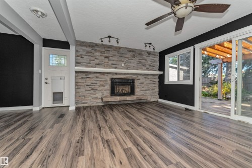 Wood-finish flooring throughout, stone-clad fireplace with mantel, ceiling fan with integrated lighting, sliding glass door leading to outdoor space, and transom window above entry door - 11208 163A Avenue Nw, Edmonton, AB 