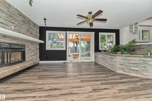 Stacked stone fireplace with hearth, wood-finish flooring, sliding glass door, and ceiling fan - 11208 163A Avenue Nw, Edmonton, AB 