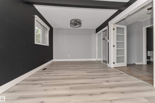 Light wood-finish flooring, ceiling-mounted fan fixture, window with white trim, built-in closet with mirrored sliding doors, and French doors with frosted glass panels - 11208 163A Avenue Nw, Edmonton, AB 