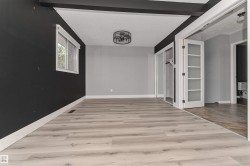 Light wood-finish flooring, ceiling-mounted fan fixture, window with white trim, built-in closet with mirrored sliding doors, and French doors with frosted glass panels - 