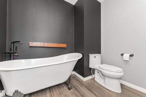Freestanding clawfoot tub with a matte black floor-mounted faucet, complemented by wood-finish flooring and a contemporary toilet - 11208 163A Avenue Nw, Edmonton, AB 