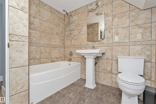 Tiled bath surround with decorative accent band, pedestal sink, chrome fixtures, and a wall-mounted mirror - 11208 163A Avenue Nw, Edmonton, AB 