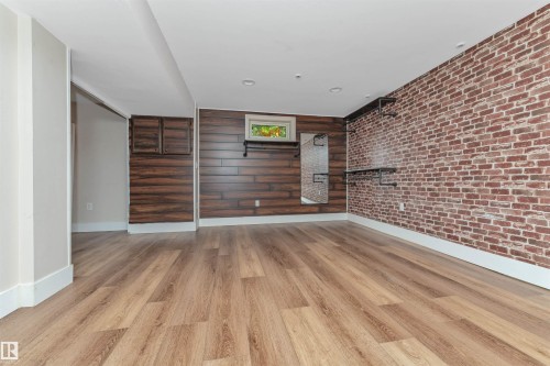 Wood-finish flooring throughout, complemented by a brick accent wall and horizontal wood-paneling - 11208 163A Avenue Nw, Edmonton, AB 