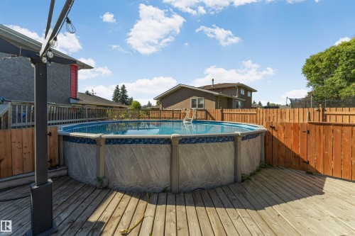 Above-ground swimming pool with an attached ladder, surrounded by wood decking and a wood privacy fence - 11208 163A Avenue Nw, Edmonton, AB 