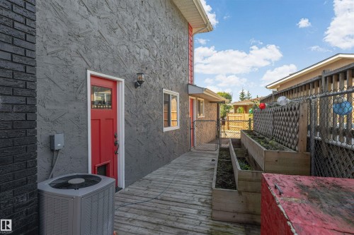 Exterior featuring a red entry door, stucco siding, black brick chimney, and a wooden deck with built-in planters - 11208 163A Avenue Nw, Edmonton, AB 