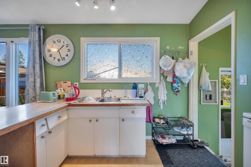 Wood-finish countertop with stainless steel sink, white cabinetry with silver-tone hardware, and a white-framed window - 8812 135A Avenue Nw, Edmonton, AB 