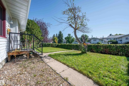 Front exterior featuring white siding, a small porch with black metal railings, a concrete walkway, and a manicured lawn - 8812 135A Avenue Nw, Edmonton, AB 