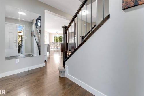 Wood-finish flooring throughout, dark wood staircase with metal balusters, white paneled entrance door, and recessed lighting - 136 55 Street Sw, Edmonton, AB 
