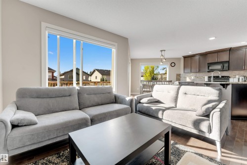 Large window with white trim, wood-finish flooring, dark wood cabinetry, stainless steel sink, and light-toned backsplash - 136 55 Street Sw, Edmonton, AB 
