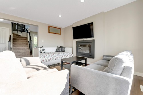 Built-in electric fireplace with a dark surround, wall-mounted television, recessed ceiling lighting, and wood-finish flooring - 136 55 Street Sw, Edmonton, AB 