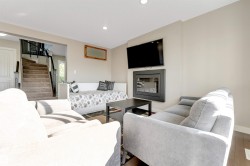 Built-in electric fireplace with a dark surround, wall-mounted television, recessed ceiling lighting, and wood-finish flooring - 