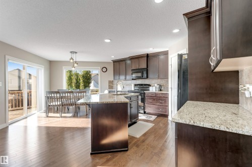 Kitchen featuring wood-finish flooring, dark wood cabinetry, granite countertops, and a tile backsplash - 136 55 Street Sw, Edmonton, AB 