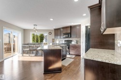 Kitchen featuring wood-finish flooring, dark wood cabinetry, granite countertops, and a tile backsplash - 