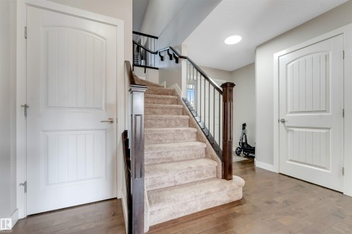 Wood-finish flooring, carpeted staircase, dark wood newel post, metal balusters, and white panel doors - 136 55 Street Sw, Edmonton, AB 