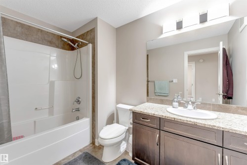 Bathtub with an integrated shower, tiled shower surround, vanity with a light-toned countertop, integrated sink, and an expansive mirror - 136 55 Street Sw, Edmonton, AB 