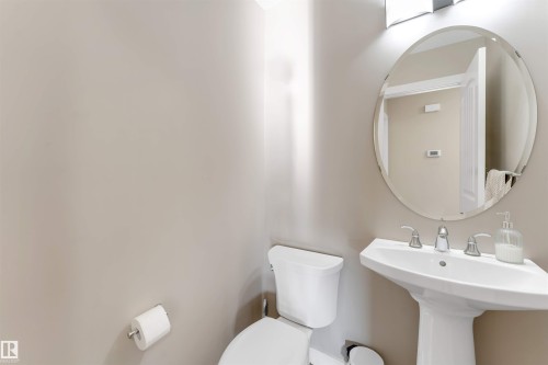 Pedestal sink with chrome fixtures and an oval, frameless mirror - 136 55 Street Sw, Edmonton, AB 