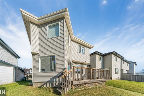 Exterior featuring siding, multiple windows, a wooden deck with railing, and a sloped lawn - 136 55 Street Sw, Edmonton, AB 