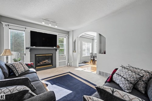 Living area featuring a fireplace with a dark mantel, track lighting, and an arched doorway - 8513 156 Avenue Nw, Edmonton, AB 
