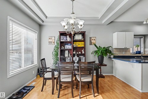Tray ceiling with a chandelier, wood-finish flooring, white upper cabinetry, and a kitchen island with a dark countertop - 8513 156 Avenue Nw, Edmonton, AB 