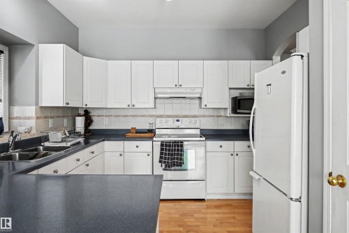 Kitchen featuring white cabinetry, dark countertops, a tile backsplash, and wood-finish flooring - 8513 156 Avenue Nw, Edmonton, AB 