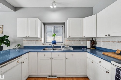 White cabinetry, blue countertops, tile backsplash, stainless steel sink, and wood-finish flooring - 8513 156 Avenue Nw, Edmonton, AB 