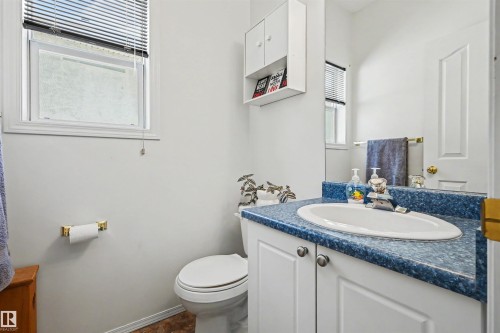 Vanity with white cabinetry and blue patterned countertop, integral sink, wall-mounted storage cabinet, and window with blinds - 8513 156 Avenue Nw, Edmonton, AB 