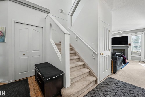 Carpeted staircase with white railings, tile flooring, and a fireplace with a mantel - 8513 156 Avenue Nw, Edmonton, AB 