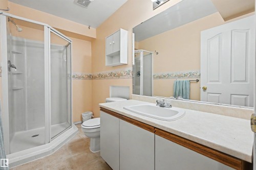 Shower enclosure with clear glass, vanity with an integrated sink, built-in storage cabinet, and a full-width mirror - 8513 156 Avenue Nw, Edmonton, AB 