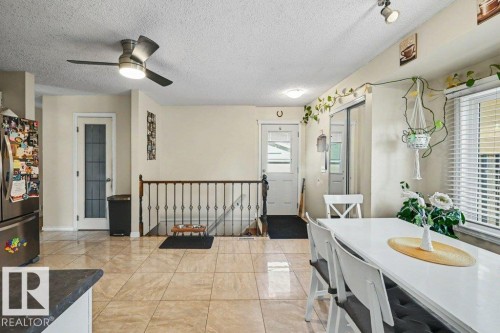Neutral-toned tile flooring, stainless steel refrigerator, white paneled door with frosted glass, ceiling fan with integrated lighting, and a window with horizontal blinds - 8708 25A Avenue Nw, Edmonton, AB 