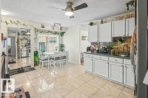 Kitchen and dining area featuring tile flooring, white cabinetry, a dark countertop, and a window with blinds - 8708 25A Avenue Nw, Edmonton, AB 