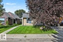 Stone facade with a sloped roofline, featuring a manicured front lawn and mature landscaping - 8708 25A Avenue Nw, Edmonton, AB 