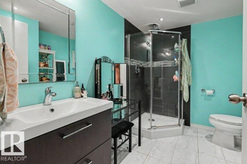 Bathroom featuring a single vanity, a frameless mirror, a corner shower enclosure, and a toilet - 8708 25A Avenue Nw, Edmonton, AB 